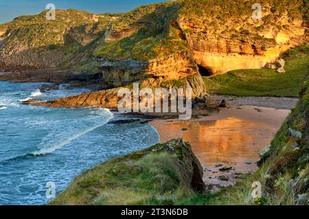 Hopeman Moray Coast Scozia sole e riflessi di una scogliera di arenaria dorata sulla spiaggia sabbiosa Foto Stock