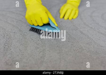 concetto di pulizia - mani in guanti di gomma gialli per la pulizia di tappeti grigi con spazzolina, spazio per la copia sul tappeto Foto Stock