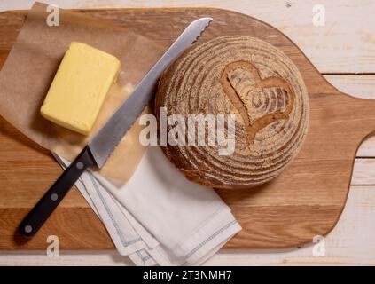 Disporre un boule di pasta madre senza glutine a forma di cuore, posizionato su un breadboard di legno con un blocco di burro. Foto Stock