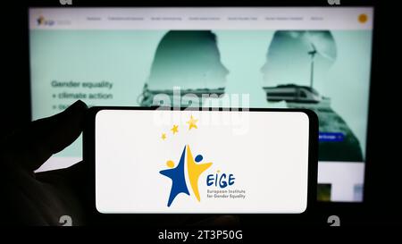 Persona che possiede uno smartphone con il logo dell'Istituto europeo per l'uguaglianza di genere (EIGE) davanti al sito web. Concentrarsi sul display del telefono. Foto Stock