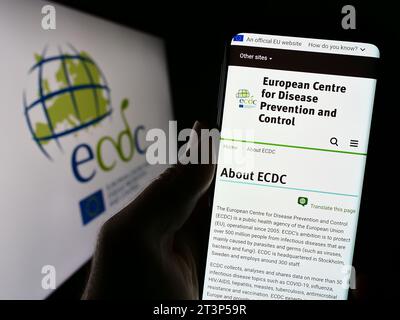 Persona in possesso di smartphone con sito web del Centro europeo per la prevenzione e il controllo delle malattie (ECDC) con logo. Concentrarsi sul centro del display del telefono. Foto Stock