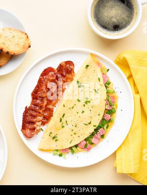 Omelette farcite con prosciutto e cipolla verde e tazza di caffè su sfondo chiaro. Pasto gustoso e salutare per colazione. Vista dall'alto, base piatta. Foto Stock