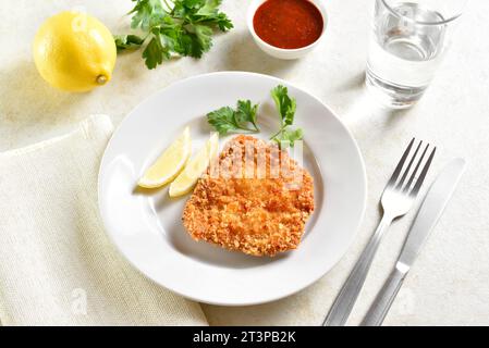 Schnitzel di pollo impanato fatto in casa con fette di limone e foglie di prezzemolo sul piatto su fondo di pietra chiaro. Vista ravvicinata Foto Stock