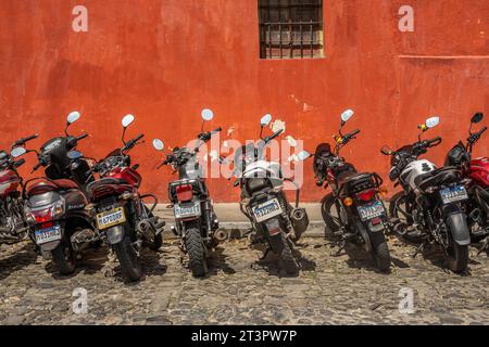 Guatemala, la Antigua - 20 luglio 2023: Motocicletta per pendolari parcheggiata di fila 8 sul lato della strada del centro, di fronte al muro rosso Foto Stock