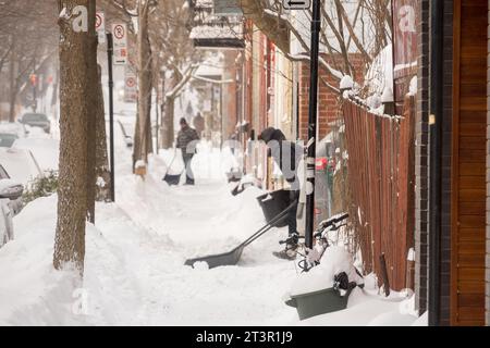 Gli uomini puliscono la neve dai loro vialetti d'inverno, dopo una tempesta di neve sull'altopiano Mont-Royal, a Montreal, provincia di Quebec, Canada. Foto Stock