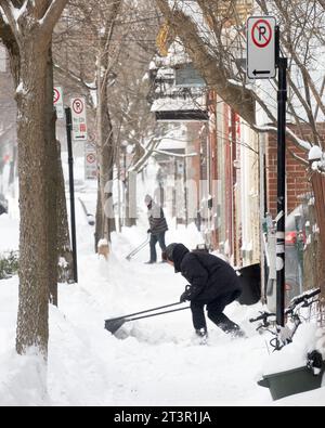 Gli uomini puliscono la neve dai loro vialetti d'inverno, dopo una tempesta di neve sull'altopiano Mont-Royal, a Montreal, provincia di Quebec, Canada. Foto Stock