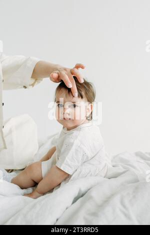 Ritratto di una bambina seduta accanto a sua madre sul letto la mattina dopo il sonno. Mamma raddrizza una ciocca di capelli per sua figlia. Co. Famiglia Foto Stock