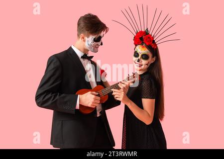 Giovane coppia vestita per il giorno dei morti del Messico (El dia de Muertos) che suona la chitarra su sfondo rosa Foto Stock