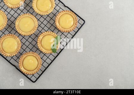 Mini crostate con ripieno di limone e crema pasticcera su griglia in metallo nero sul tavolo da cucina, vista dall'alto Foto Stock