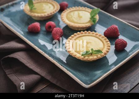 Mini crostate con ripieno di limone e crema pasticcera su tavola rustica in legno per primo piano Foto Stock