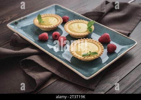 Mini crostate con ripieno di limone e crema pasticcera su tavola rustica in legno per primo piano Foto Stock