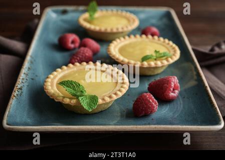 Mini crostate con ripieno di limone e crema pasticcera in piatto blu su fondo di legno Foto Stock