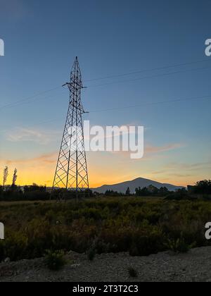 Tralicci aerei, tralicci ad alta tensione in prato con montagne sullo sfondo al tramonto estivo, vicino a Oricum, Albania Foto Stock