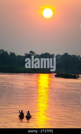 Sagome di due figure umane in kayak, che attraversano le calme e tranquille acque del Mekong, attraverso raggi di luce dorata riflessa sull'acqua, Foto Stock