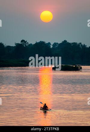 Sagoma di una figura umana in kayak, che attraversa le calme e tranquille acque del Mekong, attraverso raggi di luce dorata riflessa sull'acqua sur Foto Stock