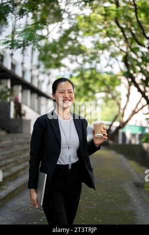 Un ritratto di una donna d'affari asiatica millenaria, bella e sicura di sé, in una tuta formale, sta camminando giù per le scale del suo edificio aziendale Foto Stock