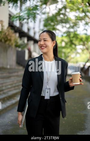 Un ritratto di una donna d'affari asiatica millenaria, bella e sicura di sé, in una tuta formale, sta camminando giù per le scale del suo edificio aziendale Foto Stock