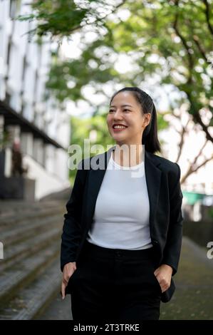 Un ritratto di una donna d'affari asiatica millenaria di successo e attraente in una tuta formale d'affari sta camminando in città. Stile di vita urbano, aziendale Foto Stock