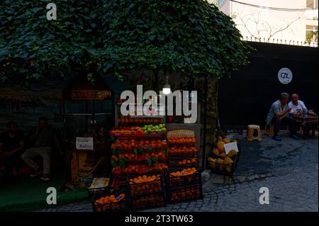 Vivace bancarella situata sotto l'ombra di un enorme albero, offre una varietà di frutta fresca e bevande rinfrescanti su una strada in pendenza. Foto Stock