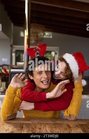 Ritratto di una coppia gay felice e diversificata che indossa cappelli di natale e che fa videochiamata a casa Foto Stock