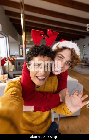 Ritratto di una coppia gay felice e diversificata che indossa cappelli di natale e che fa videochiamata a casa Foto Stock