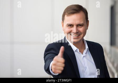 Un uomo d'affari sicuro di sé sorride e alza il pollice Foto Stock