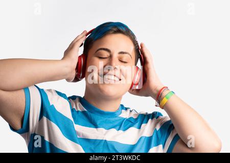 Ritratto di una giovane persona androgina con capelli colorati di colore blu brillante, che indossa cuffie e una camicia a righe. Si stanno godendo la musica, mostrando un Foto Stock