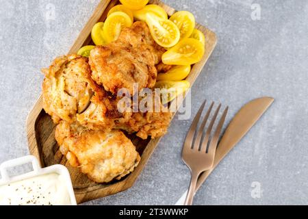 Il piatto di pesce è un filetto di merluzzo fritto con una salsa cremosa e pomodori di prugne gialli, servito su un piatto di legno a forma di pesce. Foto Stock