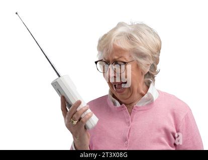 Donna anziana frustrata che usa un vecchio telefono cordless, sta gridando forte e sta parlando con una persona sorda Foto Stock