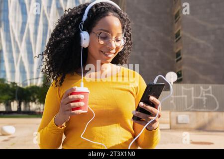 Giovane donna afroamericana sorride e digita con un'applicazione per smartphone. Foto Stock
