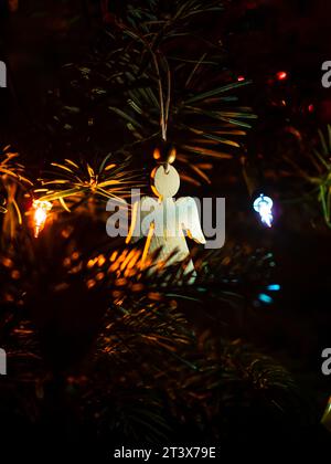 Primo piano dell'ornamento di un angelo di legno dell'albero di Natale tra rami di pino e luci di Natale Foto Stock