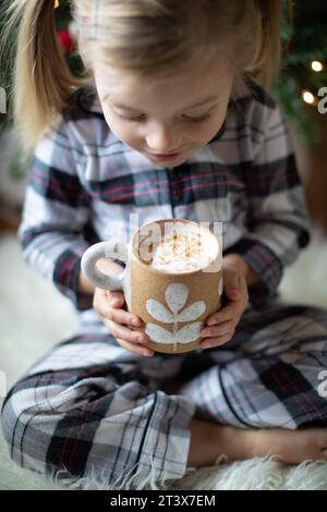 La ragazza gioiosa (3) tiene la tazza di cacao, guardando con entusiasmo verso il basso. Foto Stock