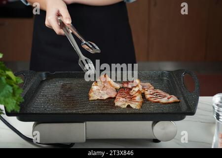 La donna sta preparando il bacon in padella. Concetto di colazione Foto Stock