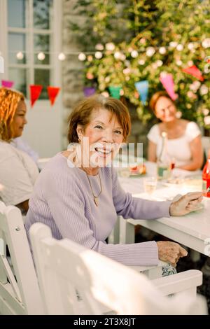 Ritratto di una donna anziana felice seduta al tavolo da pranzo nel cortile posteriore Foto Stock