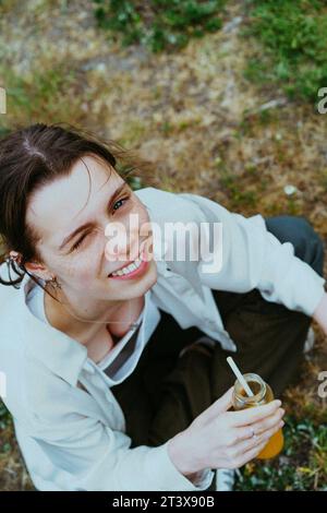 Ritratto ad alto angolo di una giovane persona non binaria sorridente che tiene una bottiglia di succo Foto Stock