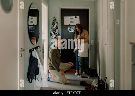 Ragazzo che abbraccia la madre con il padre inginocchiato nel fango a casa Foto Stock