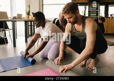 Colleghi multirazziali che girano stuoie yoga sul posto di lavoro Foto Stock