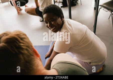 Donna d'affari sorridente che rotola il tappetino yoga da un collega maschio sul posto di lavoro Foto Stock