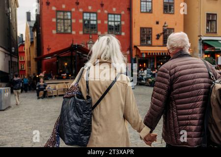 Vista posteriore della coppia anziana che si tiene per mano mentre cammina insieme in città Foto Stock