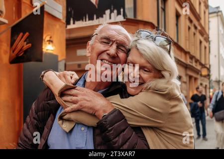 Donna anziana felice che abbraccia un uomo da dietro in città Foto Stock