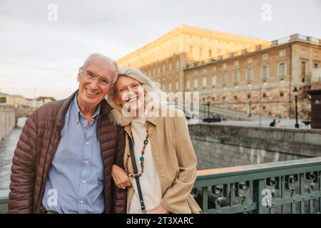 Ritratto di uomo e donna anziano felici appoggiati su una ringhiera in città Foto Stock