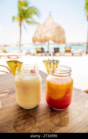 Due colorati cocktail tropicali, con un cuneo di ananas, affacciati su una soleggiata spiaggia caraibica Foto Stock