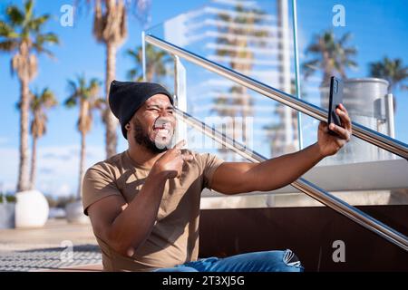 Un uomo nero felice che scatta una foto con uno smartphone. Foto Stock