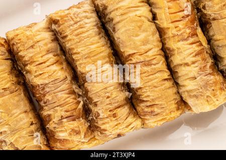 Diversi pezzi di dolce baklava su un piatto di ceramica bianca, macro, vista dall'alto. Foto Stock