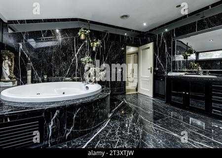 grande bagno piastrellato con marmo nero con venature nere, vasca idromassaggio circolare Foto Stock