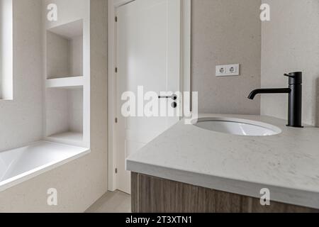 Immagine del bagno con piastrelle color crema, piano di lavoro coordinato, mobili con cassetti in legno Foto Stock