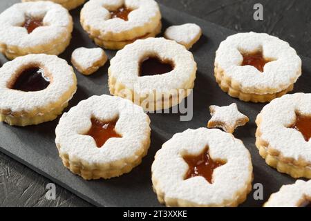 Biscotti Linzer fatti in casa cosparsi di zucchero a velo con marmellata di albicocche su sfondo nero. Prelibatezze gustose per le feste. Foto Stock