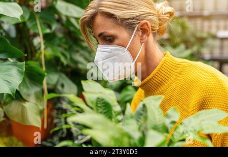 Donna in maschera che ammira una pianta Zebra in vaso in un supermercato alla pandemia di corona Foto Stock
