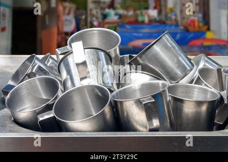 Una pila di tazze in alluminio in un lavandino in un fast food, Thailandia Foto Stock