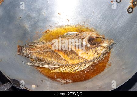 Il pesce tilapia viene fritto in olio in una padella Foto Stock